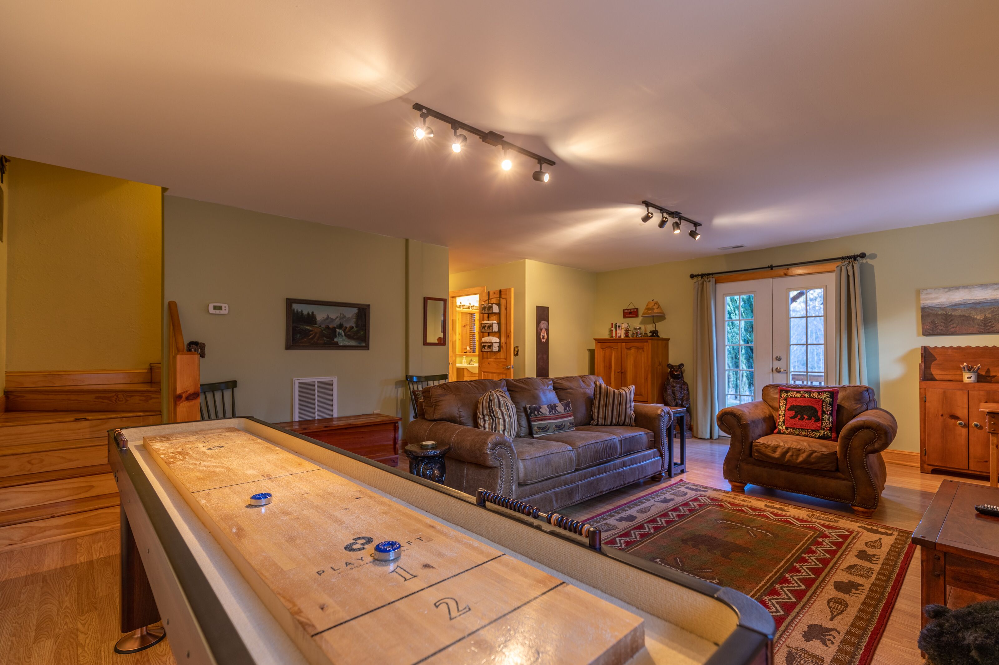 Ein gemütliches Wohnzimmer mit einem Shuffleboard-Tisch, einem braunen Ledersofa und einem Holzschrank.