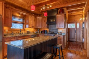 A spacious kitchen with wooden cabinets, granite countertops, and a central island with stools.