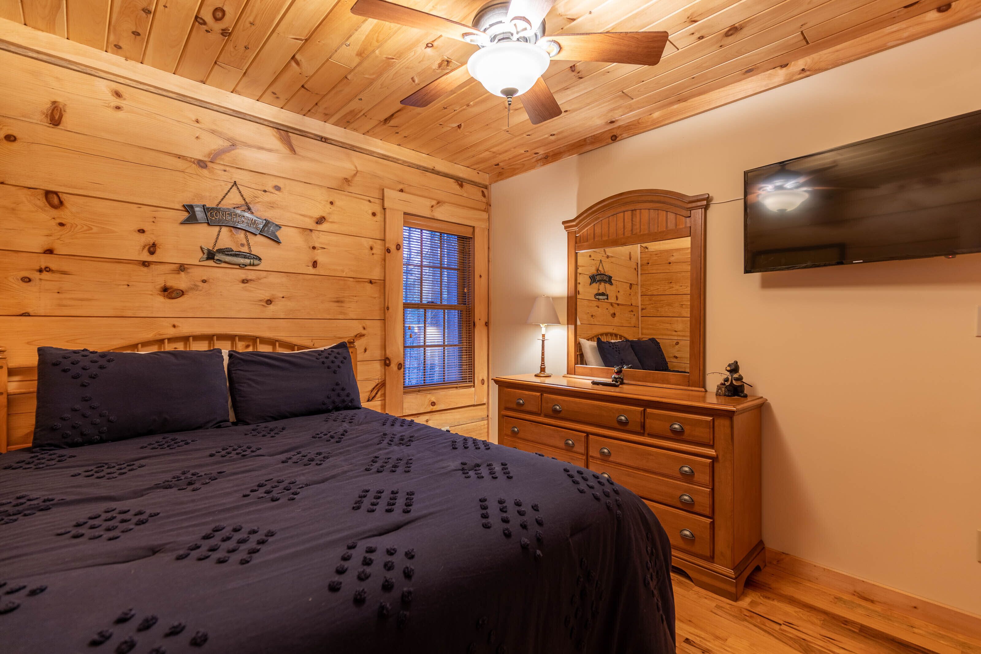 A wooden-paneled bedroom with a bed, dresser, and ceiling fan.