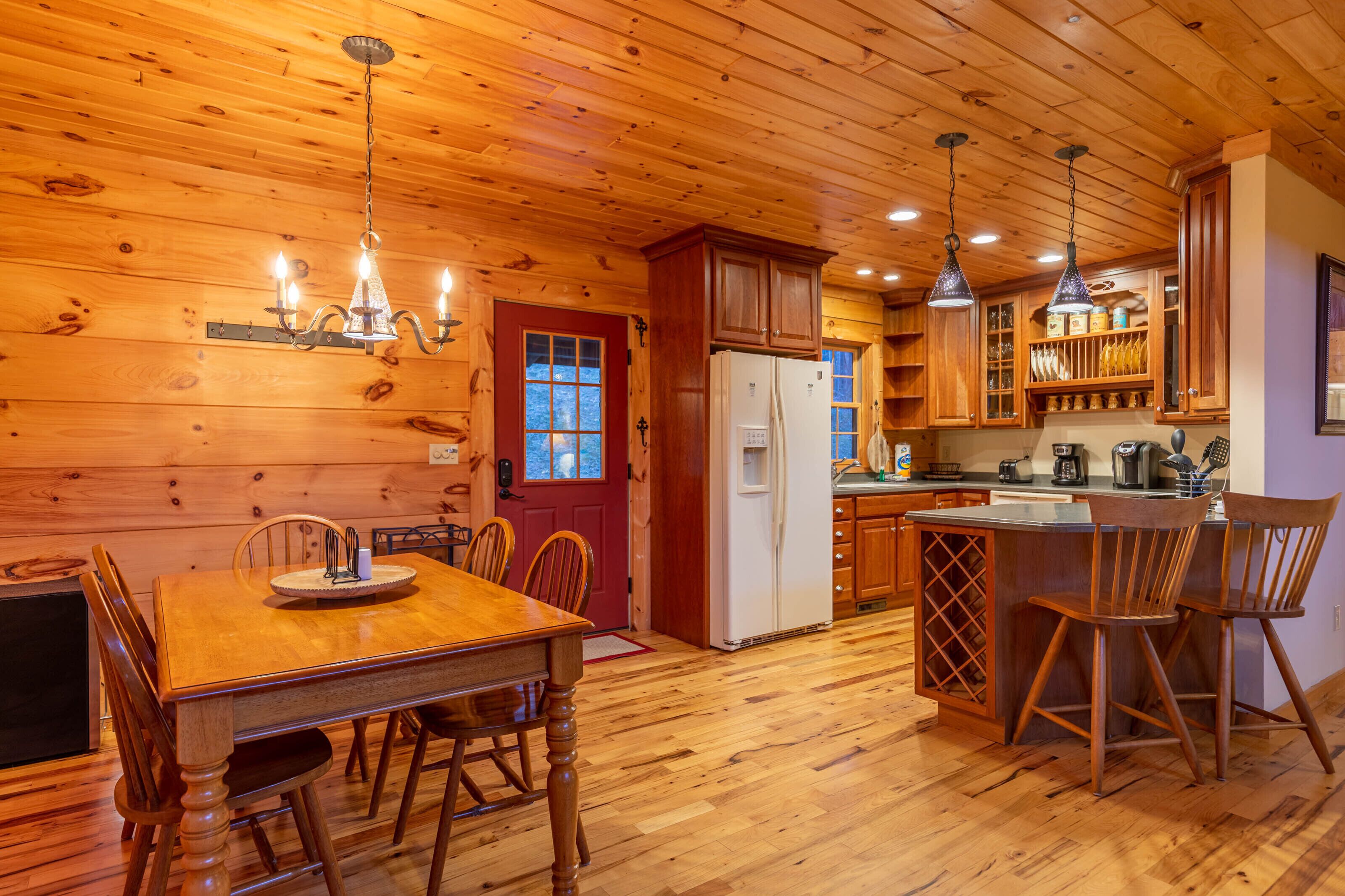 A wooden interior with a dining table, chairs, a refrigerator, and a kitchen area with cabinets and a sink.