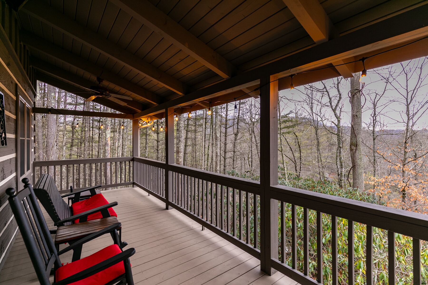 A wooden deck with a railing, two chairs, and a view of a forested area.
