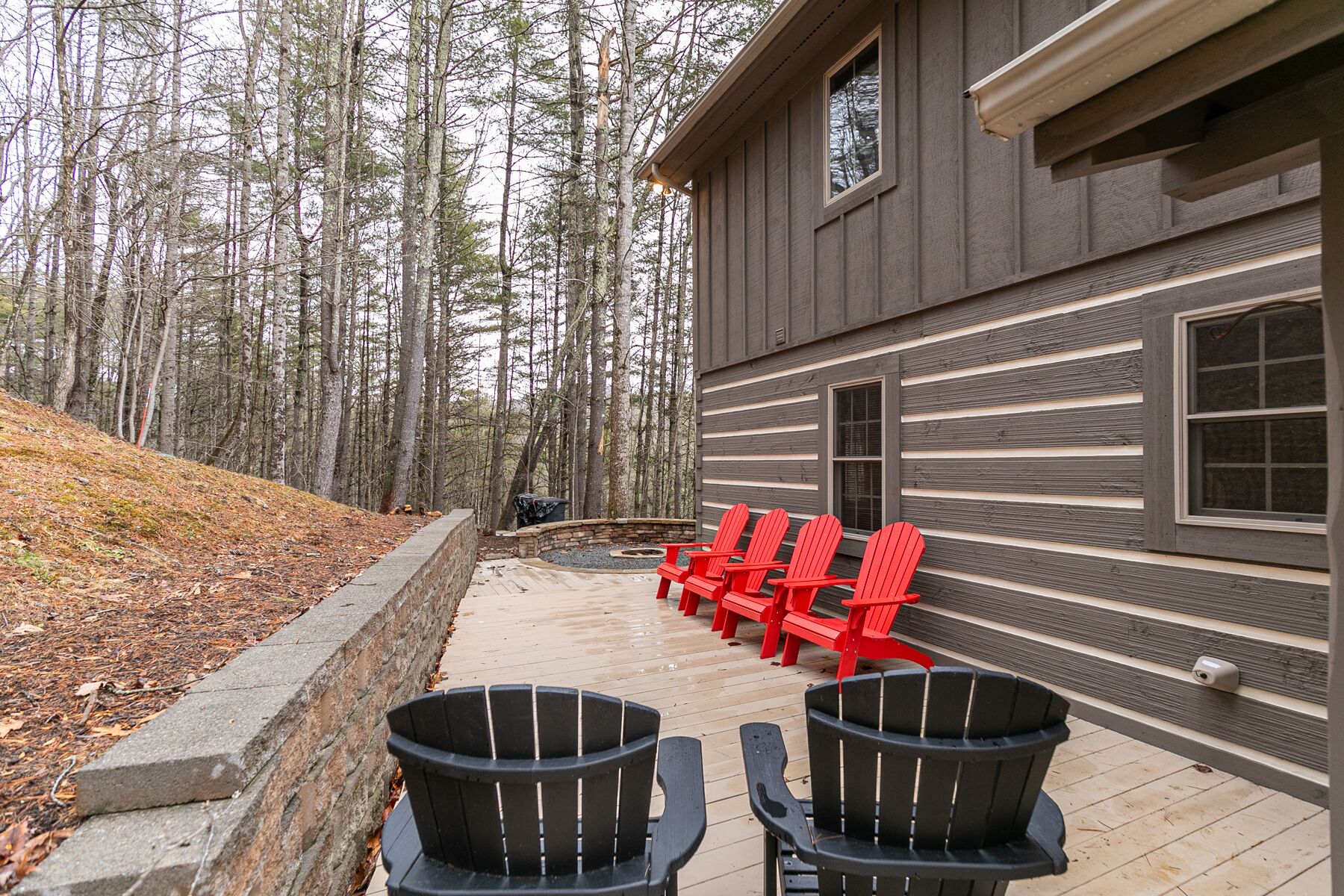 Ein Gebäude mit Holzfassade und einer Terrasse, auf der sich schwarze und rote Adirondack-Stühle befinden.