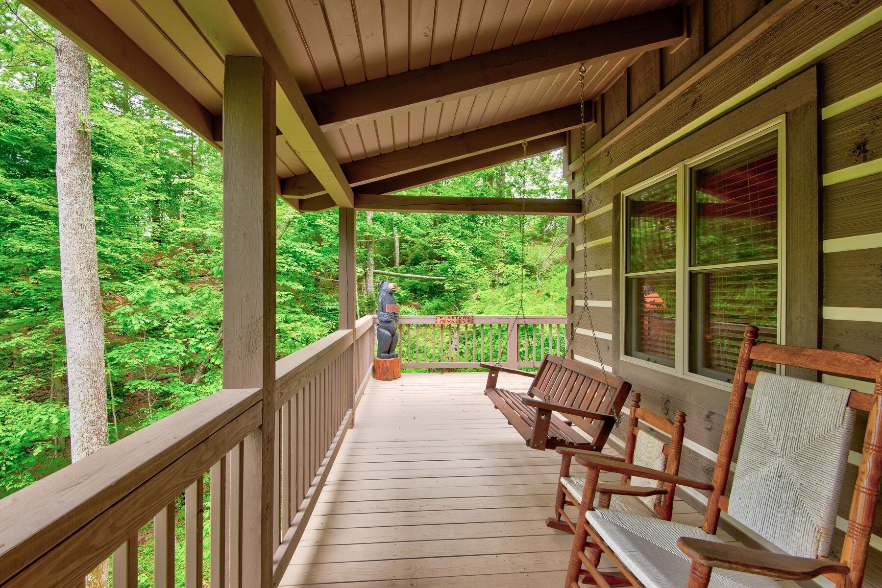 A wooden porch with a bench and a swing, overlooking a forested area.