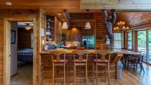 A wooden cabin interior with a kitchen, dining area, and a large bear sculpture. - Four points, mountain views, king with fireplace on main, hot tub, pet friendly (Vilas)