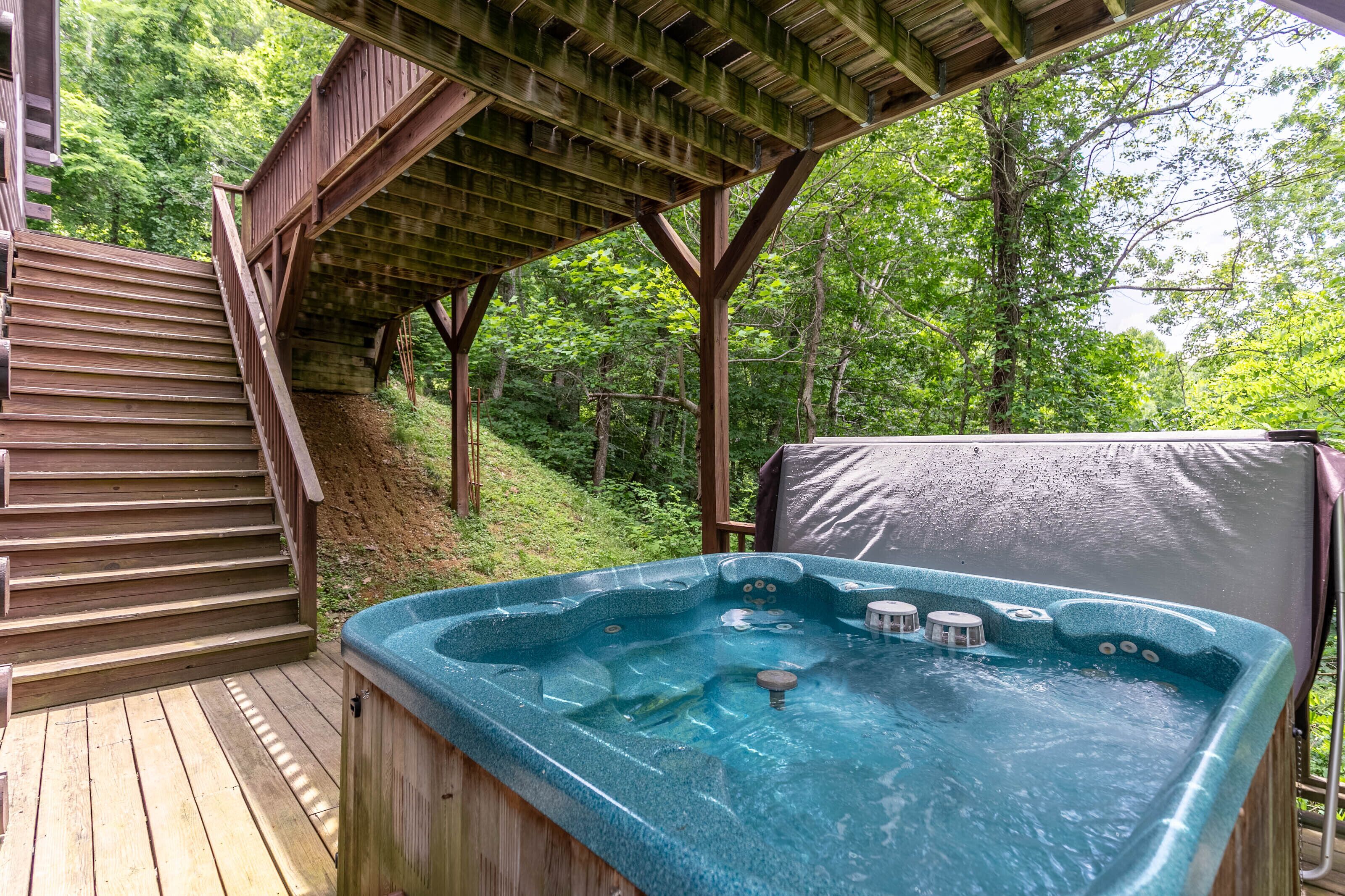 A wooden deck with a hot tub and stairs leading to a covered area.