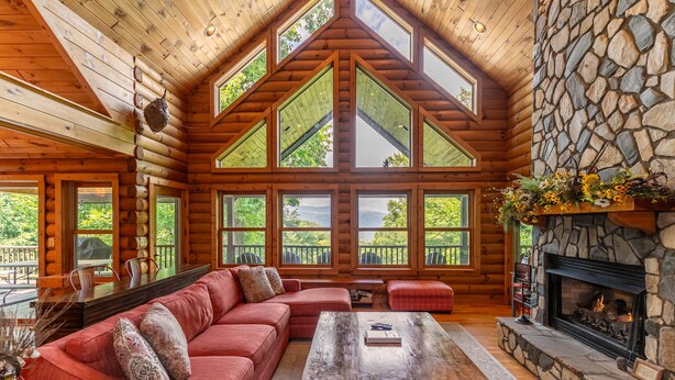 A log cabin interior with a large wooden ceiling, stone fireplace, and a cozy seating area with a red sofa and a coffee table. - Four points, mountain views, king with fireplace on main, hot tub, pet friendly (Vilas)