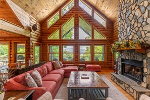 A log cabin interior with a large wooden ceiling, stone fireplace, and a cozy seating area with a red sofa and a coffee table. - Four points, mountain views, king with fireplace on main, hot tub, pet friendly (Vilas)