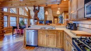 A log cabin interior with a kitchen featuring wooden cabinets, a stainless steel dishwasher, a large stove, and a stone fireplace. - Four points, mountain views, king with fireplace on main, hot tub, pet friendly (Vilas)