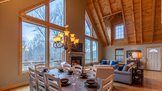 Un comedor con una mesa de madera dispuesta para seis personas, rodeada de sillas blancas, un candelabro y una chimenea.