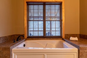Een badkamer met een ruim bad, een raam met zonwering, een handdoek op het aanrecht en een betegelde marmeren wand.
