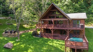 Une cabane en rondins à deux étages, dotée d’un balcon et d’une terrasse, entourée d’une pelouse bien entretenue et d’arbres.