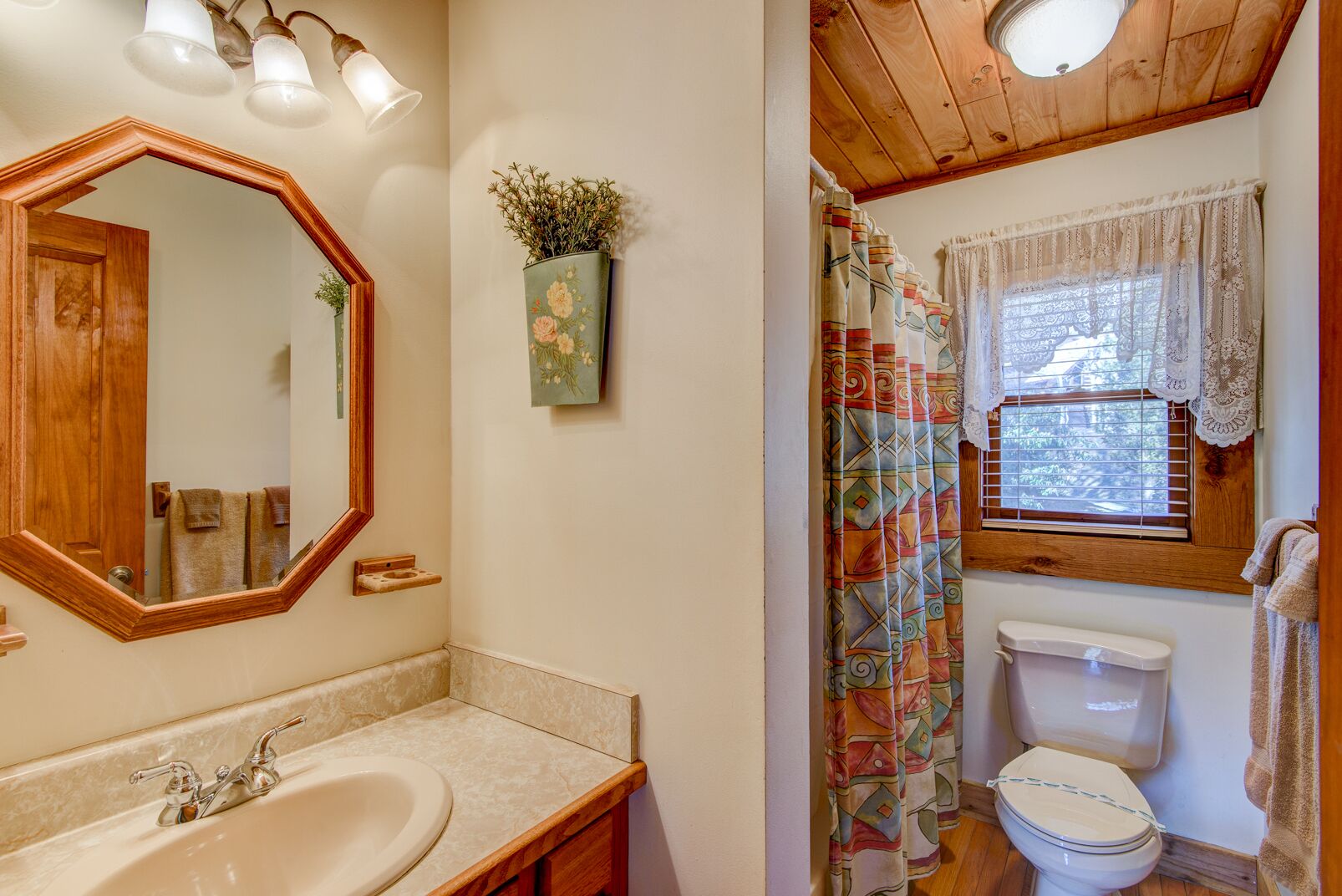 A bathroom with a wooden vanity, a sink, a mirror, a toilet, and a shower curtain.