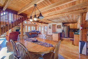 Une cabane en bois spacieuse comprenant un coin repas, une cuisine et un escalier menant à une mezzanine.