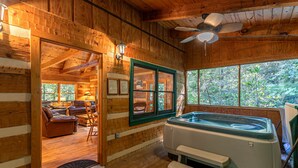 A wooden cabin interior with a hot tub, seating area, and large windows offering a view of the outdoors. - Skylark - Cozy Log Cabin with 3 bedrooms, 3 baths, and hot tub (Banner Elk)