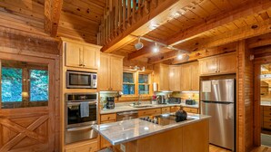 A wooden cabin-style kitchen with built-in appliances, a large island, and a view of the forest. - Skylark - Cozy Log Cabin with 3 bedrooms, 3 baths, and hot tub (Banner Elk)