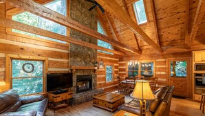 A log cabin interior with a stone fireplace, leather furniture, and large windows. - Skylark - Cozy Log Cabin with 3 bedrooms, 3 baths, and hot tub (Banner Elk)