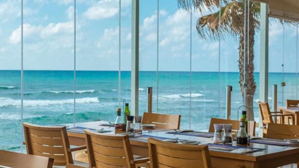 A dining area with a view of the ocean, featuring wooden tables and chairs, and a palm tree. - Mi Capricho P.5, Apartment with Sea and Pool Views (Mijas)