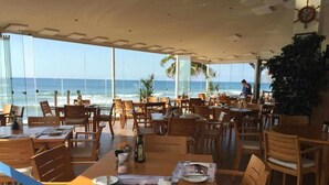 A restaurant with wooden tables and chairs, large windows overlooking the ocean, and a view of the beach. - Mi Capricho P.5, Apartment with Sea and Pool Views (Mijas)