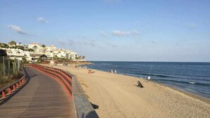 A beach with a wooden boardwalk leading to the shore, a sandy beach, and buildings in the background. - Mi Capricho P.5, Apartment with Sea and Pool Views (Mijas)