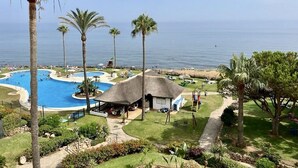 A resort with a large swimming pool, palm trees, and a beach view. - Mi Capricho P.5, Apartment with Sea and Pool Views (Mijas)