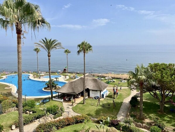 A resort with a large swimming pool, palm trees, and a beach view. - Mi Capricho P.5, Apartment with Sea and Pool Views (Mijas)