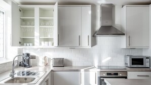 Una cocina moderna con gabinetes blancos, una campana extractora de acero inoxidable, un tostador, una cafetera y un microondas.