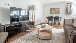 Una sala moderna con un televisor de pantalla plana, una mesa de centro, un sofá y un comedor con sillas.