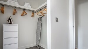 Un vestidor con un aparador blanco, una percha con colgadores de madera y una tabla de planchar plegada.