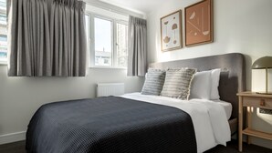 Un dormitorio ordenado con una cama grande, una mesita de noche y dos cuadros enmarcados en la pared.