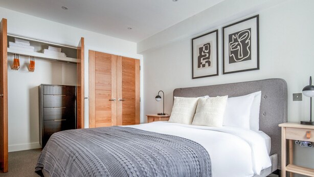 A modern bedroom with a bed, a wardrobe, a nightstand, and two framed artworks on the wall. - Deluxe Marylebone 2BR nr Oxford St, by Blueground (London)