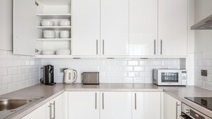 A modern kitchen with white cabinets, a stainless steel sink, a coffee maker, a toaster, and a microwave. - Deluxe Marylebone 2BR nr Oxford St, by Blueground (London)