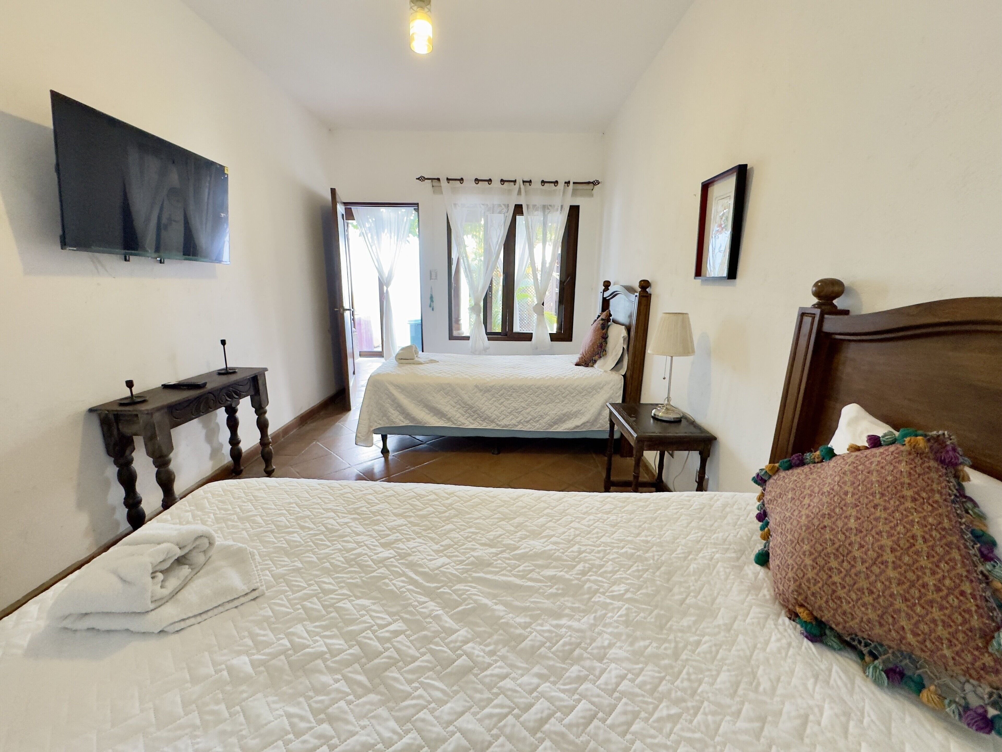 Une chambre d’hôtel avec un grand lit, une table de chevet, un téléviseur fixé au mur et une fenêtre avec des rideaux.