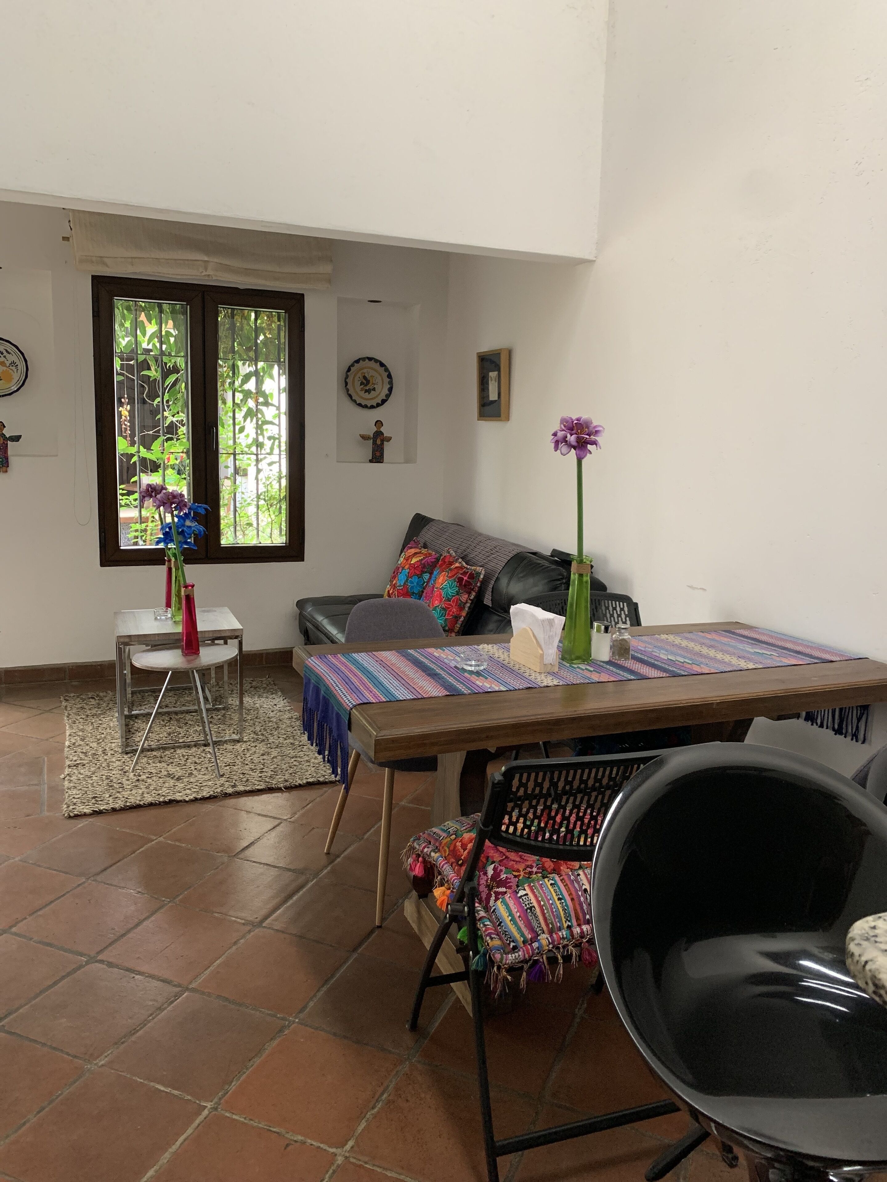 Un comedor con una mesa de madera, sillas y un tapete. Se ve una ventana con vistas a zonas verdes.