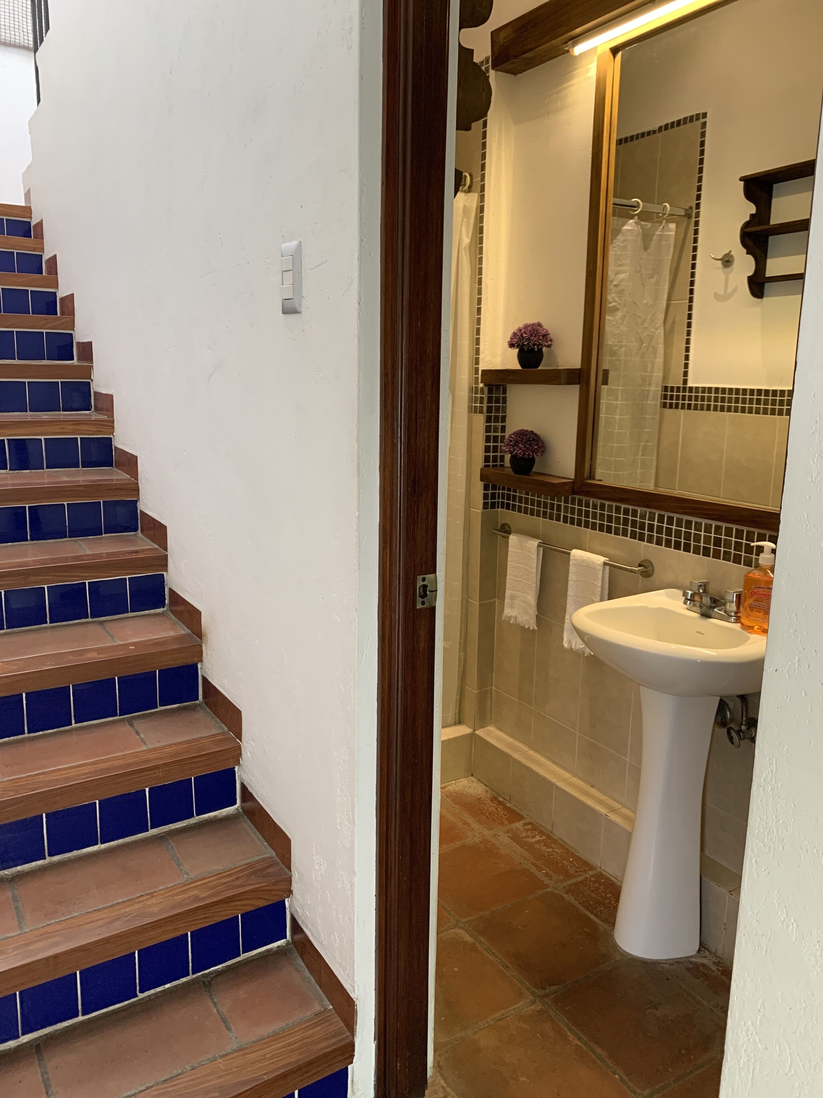 Een badkamer met een wit wastafelmeubel, een glazen douchecabine en een houten trap met blauw betegelde treden.
