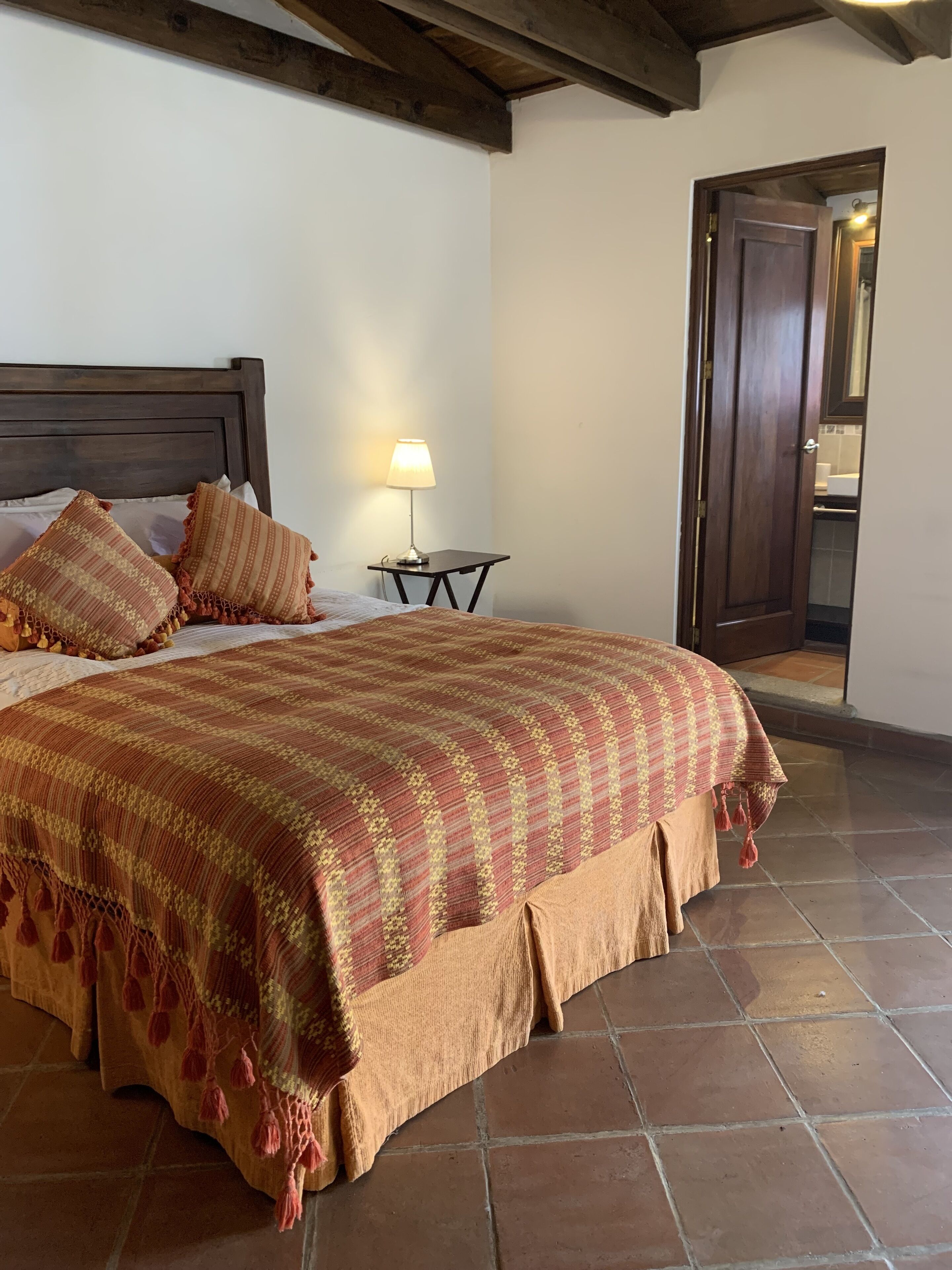 Un lit bien fait, avec une couvre-lit à motifs et des oreillers, une lampe de chevet et une porte en bois sur le côté droit.