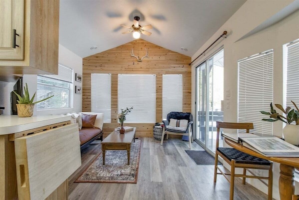 A cozy living room with wooden walls, a ceiling fan, a sofa, a coffee table, and a dining area with a chair and table. - Minimalist Hideaway | WiFi, BBQ, Smart TV (Packwood)