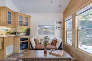 A cozy kitchen with wooden cabinets, a sofa, and a large window. - Minimalist Hideaway | WiFi, BBQ, Smart TV (Packwood)