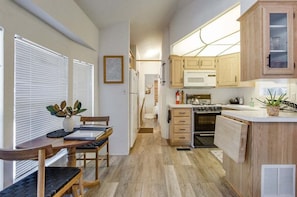 A modern kitchen with wooden cabinets, a microwave, and a stove. There is a dining area with a table and chairs.