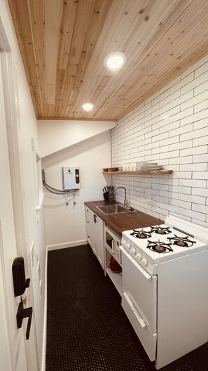 A compact kitchen with a wooden ceiling, white tiled backsplash, a gas stove, and a built-in oven.