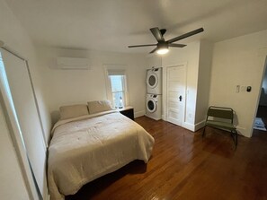 A bedroom with a bed, a ceiling fan, a washing machine, and a bench.