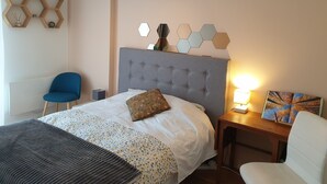 Quarto bem organizado com uma cama grande, uma cadeira, uma escrivaninha e uma estante na parede.