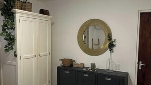 Une pièce avec une armoire blanche, une commode sombre dotée de tiroirs, un miroir rond et une porte.