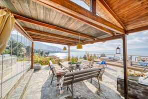 A covered outdoor seating area with stone flooring, wooden furniture, and a view of the sea. - Magical View, Villa Asproneri, Kamena Vourla (kamena)
