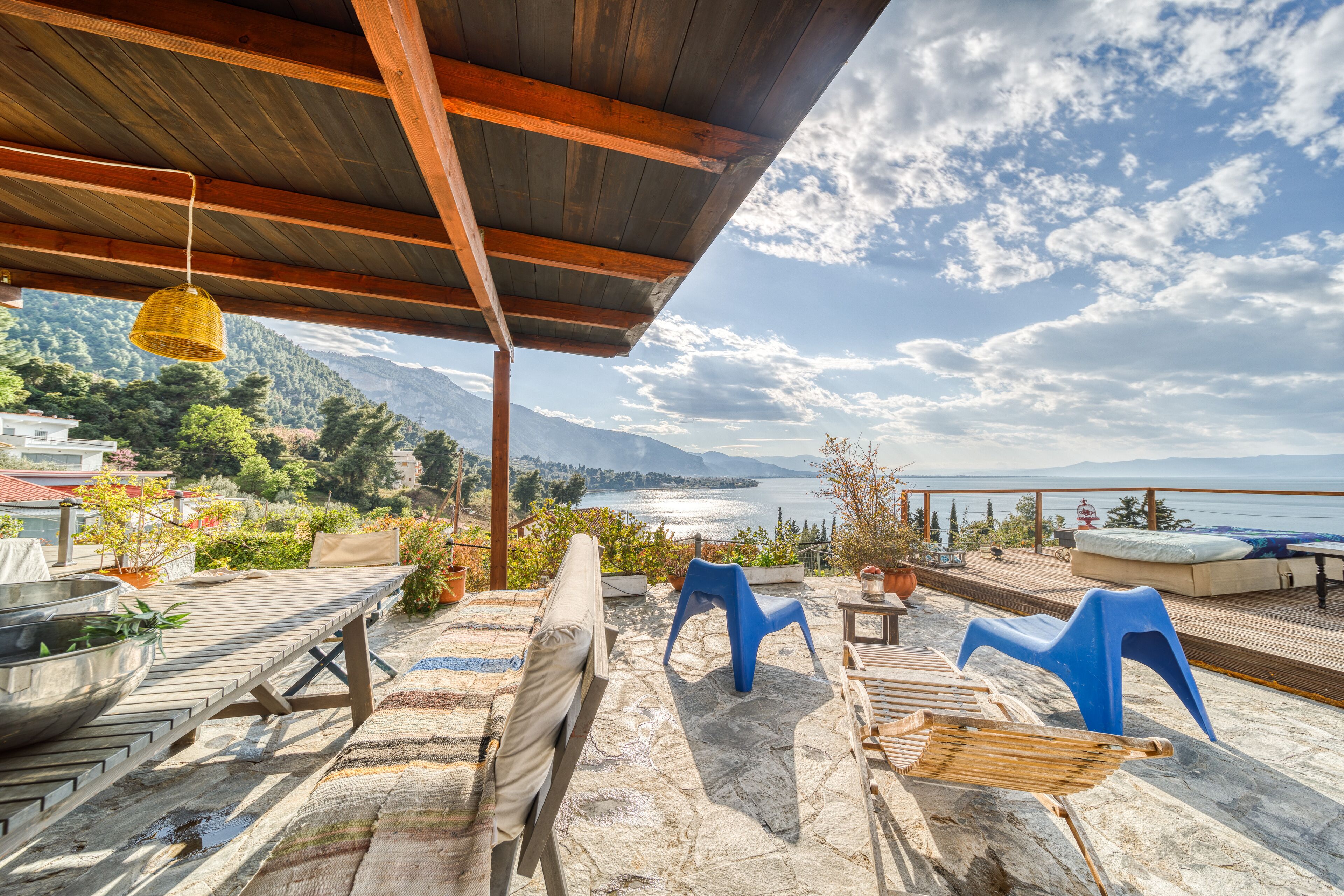 Eine Terrasse im Freien mit Holzdeck, Steinböden und Blick auf einen See und Berge.
