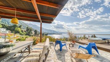 Eine Terrasse im Freien mit Holzdeck, Steinböden und Blick auf einen See und Berge.