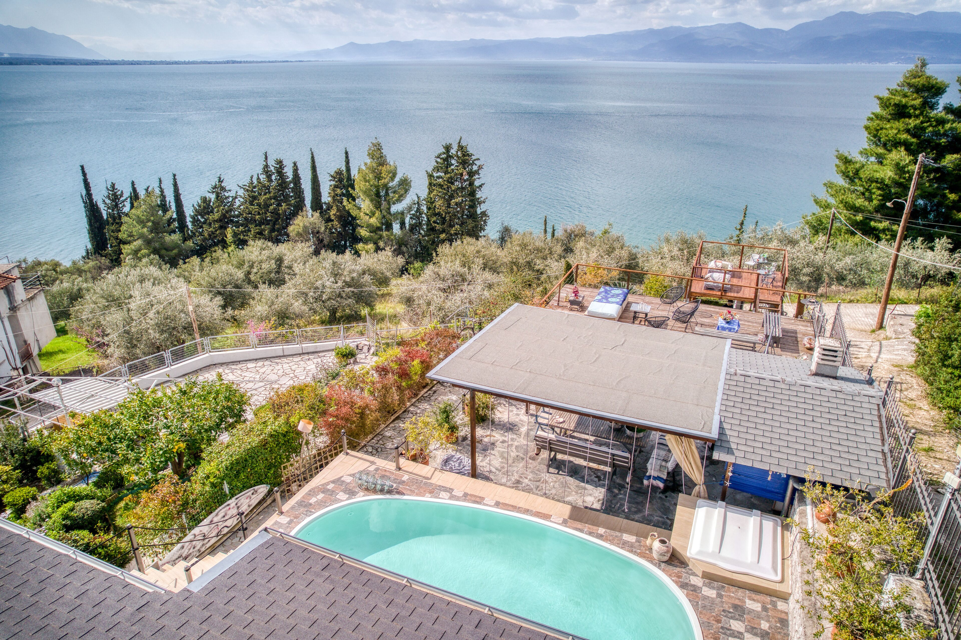 A pool area with a view of a lake and mountains, surrounded by trees and a deck with outdoor seating.
