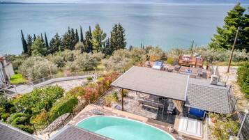 A pool area with a view of a lake and mountains, surrounded by trees and a deck with outdoor seating.