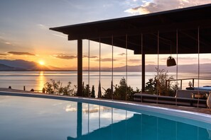 An infinity pool with a view of the sunset over a body of water, a pergola structure, and outdoor furniture. - Magical View, Villa Asproneri, Kamena Vourla (kamena)