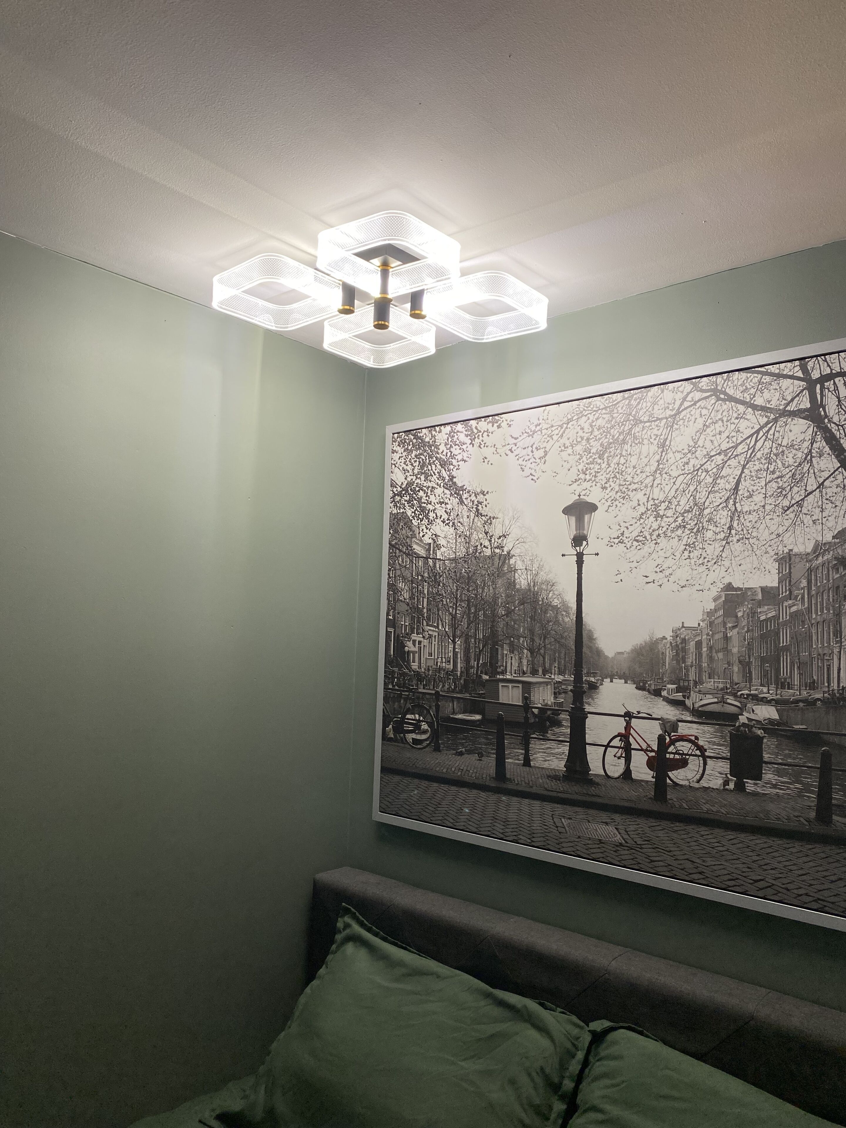 Una habitación con una cama, una pared verde y un cuadro grande de un paisaje urbano en blanco y negro.