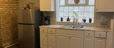 A kitchen with white cabinets, a stainless steel refrigerator, a brick wall, and a window with a view.